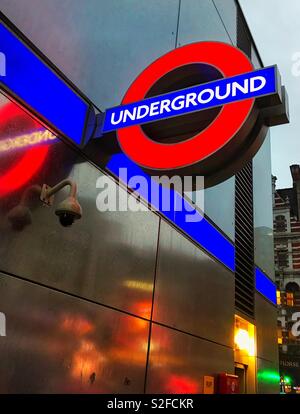 Segno al di fuori di una stazione della metropolitana di Londra in un buio, bagnato inverno di pomeriggio con le luci riflesse sulla parete Foto Stock