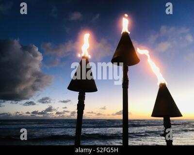 Torce Tiki al tramonto sulla spiaggia di un resort. Poipu, Kauai USA. Foto Stock