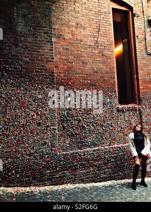 Giovane donna soffiando bubble gum nella parte anteriore della gengiva coperta parete in Post Alley di Seattle Foto Stock