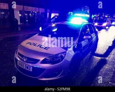 Auto della Polizia parcheggiata su una strada di città di notte con luci blu lampeggiante Foto Stock