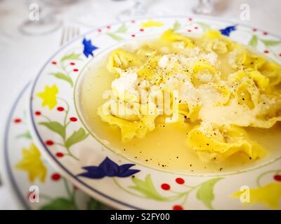 Vista ravvicinata di un piatto di zuppa con cappelletti in brodo di pollo e parmigiano grattugiato sulla sommità. piatto tipico della regione Emilia Romagna in Italia Foto Stock