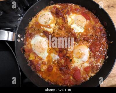 Shakshouka o shakshuka, medio orientale colazione piatto di uova in camicia in un pomodoro, peperoncino e cipolla salsa. Foto Stock