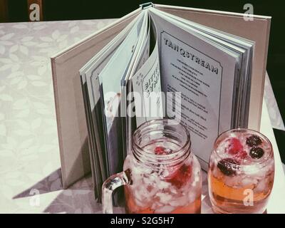 Due gin colorati cocktail accanto a un libro di ricette per cocktail - su un tavolo. Foto Stock