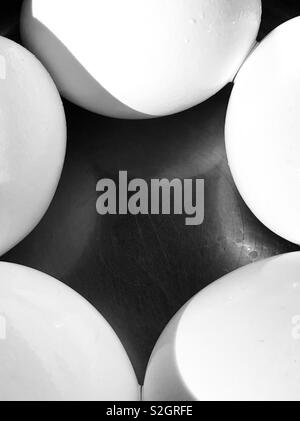 Cinque uova di colore bianco su una superficie nera creando un riassunto Foto Stock