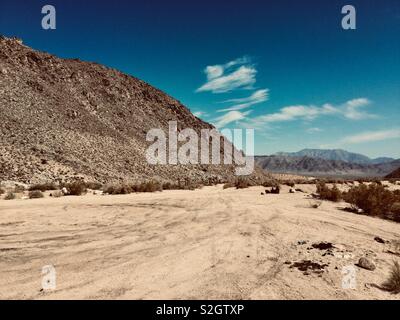 Hot Dry lonely deserto sotto luminose blu cielo con soffici nuvole e montagne brulle. Foto Stock