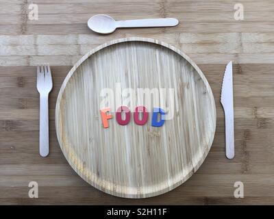 Piatto di legno con posate di legno su una tavola di legno abd di legno colorato lettere della parola cibo Foto Stock