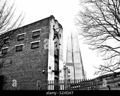 Il vecchio e il nuovo. Un capannone abbandonato nei pressi del moderno, Nebbia avvolta in acciaio e vetro di Shard edificio vicino al London Bridge, Londra , Inghilterra Foto Stock