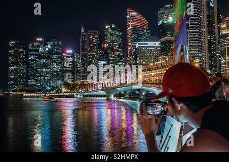 Tourist fotografare la notte di Singapore cityscape con la fotocamera del cellulare. Foto Stock