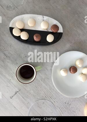 Cioccolato fondente e bianco macarons su nero un marmo bianco vassoio sul tavolo da caffè in legno Foto Stock