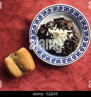 I fagioli neri con il formaggio in ceramica decorata piastra e un pezzo di pane su una tabella rossa in Santa Clara ristorante a Puebla, in Messico Foto Stock