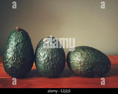 Closeup ancora la vita di tre avocado su una superficie in legno con sfondo grigio Foto Stock