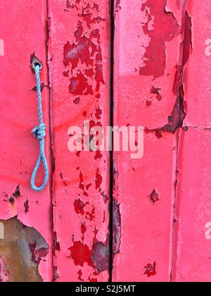 Peeling sbiadita della vernice rossa su una vecchia porta di garage. Foto Stock