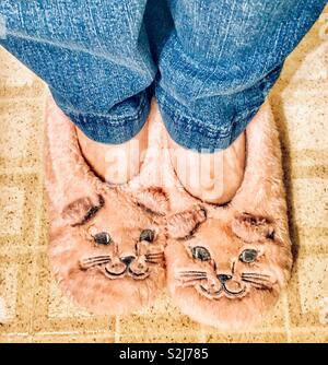 I piedi di una ragazza jeans blu e rosa Fuzzy kitty pantofole sul pavimento di piastrelle Foto Stock