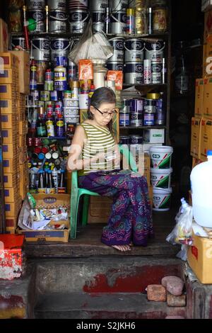 Ritratto di una donna birmana. vecchia signora in Myanmar, che posano per una foto nel suo piccolo negozio per i colori e la vernice in Yangon, Birmania. Contando il suo fatturato quotidiano. Foto Stock