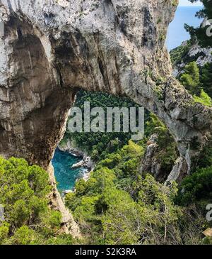 Guardando verso il basso su di una piccola baia del Mar Mediterraneo attraverso la formazione di roccia Arco Naturale, Capri, Italia Foto Stock