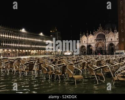 Piazza San Marco è sotto l'acqua, cafe tavolo e sedie gialle sommersa. Immagine di notte e le luci sono riflettenti in acqua Foto Stock