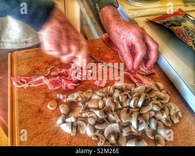 L uomo per affettare la pancetta e funghi su estrarre il tagliere in svedese di cucina domestica, Svezia e Scandinavia Foto Stock