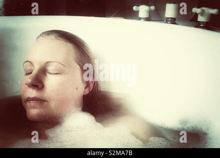 Donna relax nel bagno di bolle con gli occhi chiusi Foto Stock