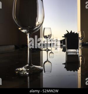 Bicchieri di vino e piante in vasi di vetro riflettente sulla tabella nel tardo pomeriggio con sky passando al crepuscolo attraverso la finestra Foto Stock