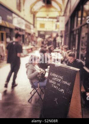 "Costoso hipster caffè servito in piccoli bicchieri" scritta su un cartello fuori un cafè nel villaggio di Brixton, Londra, Inghilterra. Foto Stock