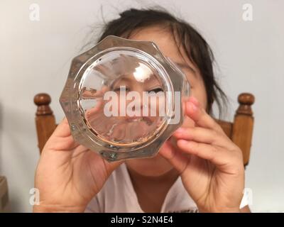 La faccia di un giovane multi-etnico (Caucasica/Punjabi/vietnamita) ragazza cerca attraverso un bicchiere. Foto Stock