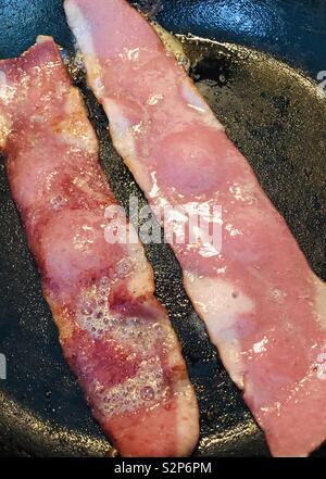 Due fette di pancetta sfrigolante in padella Foto Stock