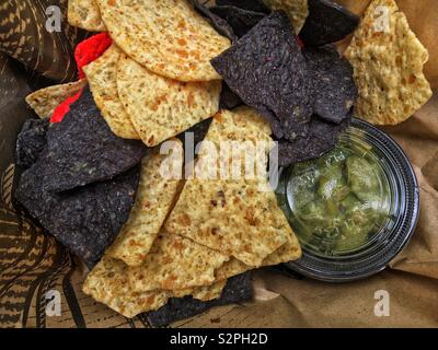 Varietà di rosso, blu e bianco corn chips impostato a fianco di una piccola vasca di fresco verde guacamole. Foto Stock