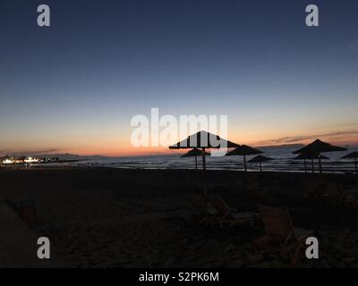 Tramonto sulla spiaggia che mostra la silhouette di ombrelloni a Creta Foto Stock