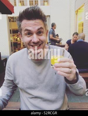 Uomo sorridente holding piccolo bicchiere di orange Foto Stock