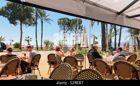 La gente seduta a tabelle in un cafe' all'aperto sul lungomare di Cannes sulla Costa Azzurra Foto Stock