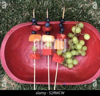 Una piastra fresca di spiedini di frutta con colorati e frutti nutritivi visualizzato su di un piatto di rosso in cantiere su un pomeriggio estati Foto Stock