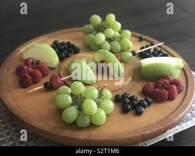 Vassoio di frutta di mele, mirtilli, lamponi, uva e servite su un piatto di legno. Foto Stock