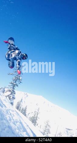 Bear Valley Ski Resort, California settentrionale. Snowboarder facendo un trick in aria su una bella giornata con cielo blu. Indossando guanti di rosso, nero e bianco giacca. Foto Stock