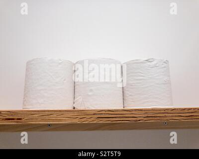 Tre rotoli di carta igienica su uno scaffale di legno contro un muro bianco . Foto Stock