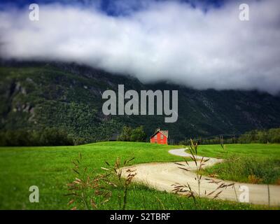 Una strada tortuosa per un rosso agriturismo ai piedi di una montagna in Norvegia Foto Stock