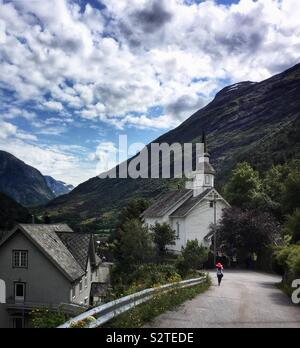 La donna in un Red Hat per raggiungere a piedi la chiesa sulla strada di un paese in Norvegia Foto Stock