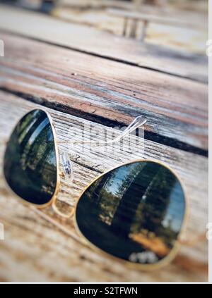 Aviator occhiali da sole seduto su un picnic in legno Tabella che mostra la riflessione degli alberi della foresta sulla lente Foto Stock