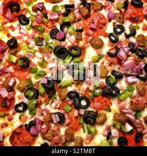 Un primo piano di una pizza con formaggio salsiccia per pizza, olive nere, prosciutto e i peperoni verdi e salsiccia Foto Stock