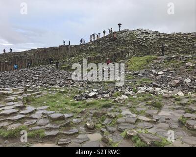 Bushmills, Irlanda del Nord- Giugno 5, 2019: colonne di basalto sono mostrati in un giorno di pioggia, con turisti arrampicata su insolite formazioni geologiche. Foto Stock