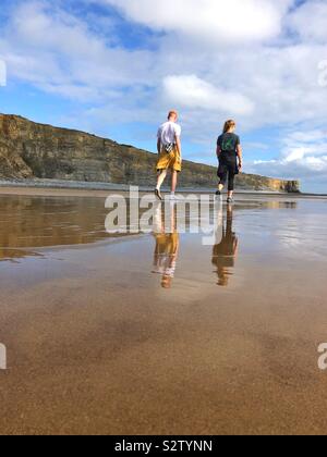 Due giovani camminando lungo una spiaggia con riflessi nella sabbia bagnata, il Galles. Foto Stock