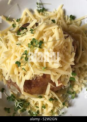 Giacca riempito di patate con formaggio di maggiore e guarnita con verde crescione. Servita su una piastra bianca Foto Stock