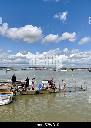 Felixstowe Ferry, Suffolk, Regno Unito - 19 August 2019: persone attività di pesca del granchio dal molo nel fiume Deben. Luminosa e soleggiata e pomeriggio. Foto Stock