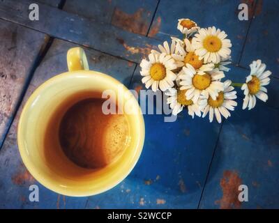 Giallo tazza da caffè e nosegay delle margherite su un dipinto di blu superficie in legno Foto Stock