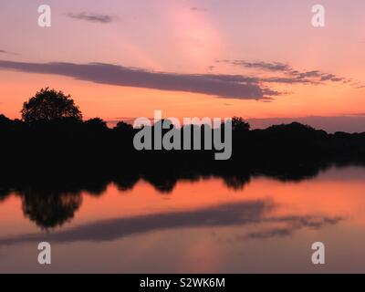 Silhouette di alberi e lago di riflessioni al tramonto Foto Stock