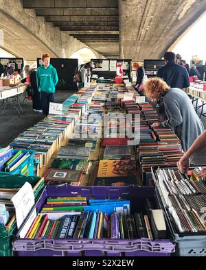 Mercato delle Pulci Prenota stallo con persone che guardano i libri sulle rive del fiume Tamigi sotto un ponte - London REGNO UNITO Foto Stock