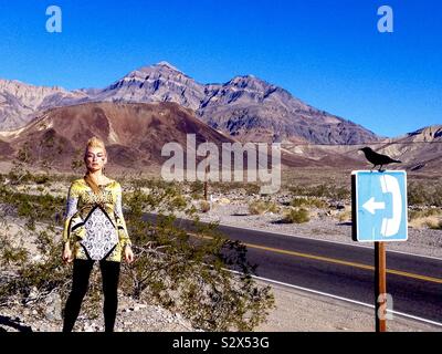 Blonde modello nella Valle della Morte in piedi attraverso un segno telefono con un corvo nero arroccato su di esso. Foto Stock