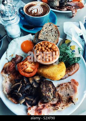 La completa prima colazione inglese fry up e un cappuccino con cuore arte Foto Stock