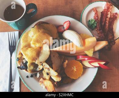 Uova Benedict con home patatine, frutta fresca, lato di pancetta e caffè Foto Stock