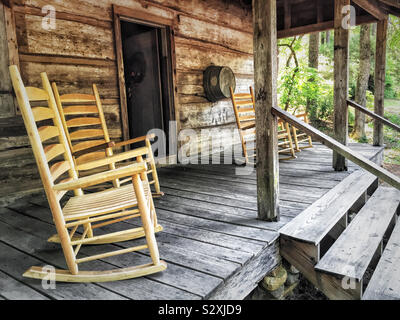 Sedie a dondolo vuote in legno sul portico anteriore di una vecchia casa in legno nel bosco. Questa casa di tronchi è stata costruita negli anni '1830 Foto Stock