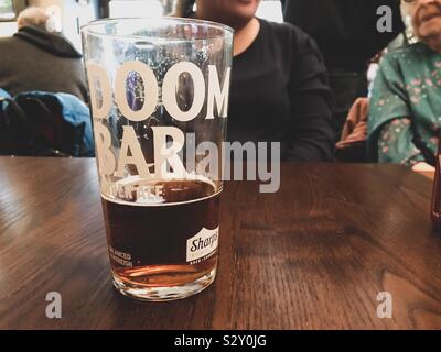 Una mezza pinta di birra ubriaco di Doom Bar ale ambrata su un tavolo. Foto Stock